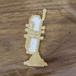 A beaded trumpet charm made out of gold and white seed beads