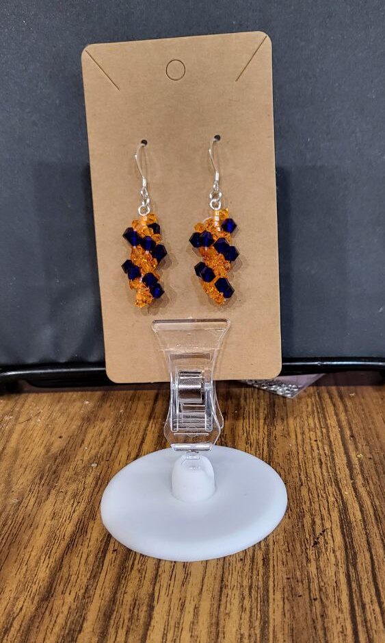pair of spiral crystal earrings on a brown card. The earrings are made of orange and blue crystals and orange seed beads
